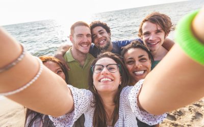 Multiracial group of friends taking selfie at beach. One girl is asiatic, two persons are black and three are caucasian. Friendship, immigration, integration and summer concepts.
